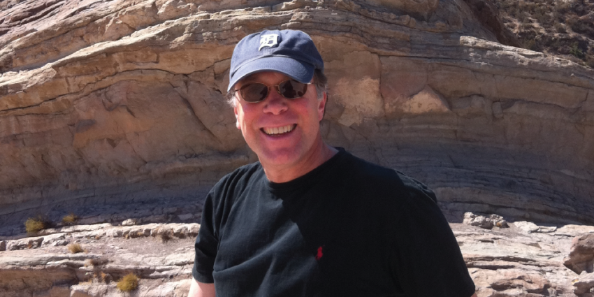 A photo of Mark Teicher smiling in front of a natural rock formation.
